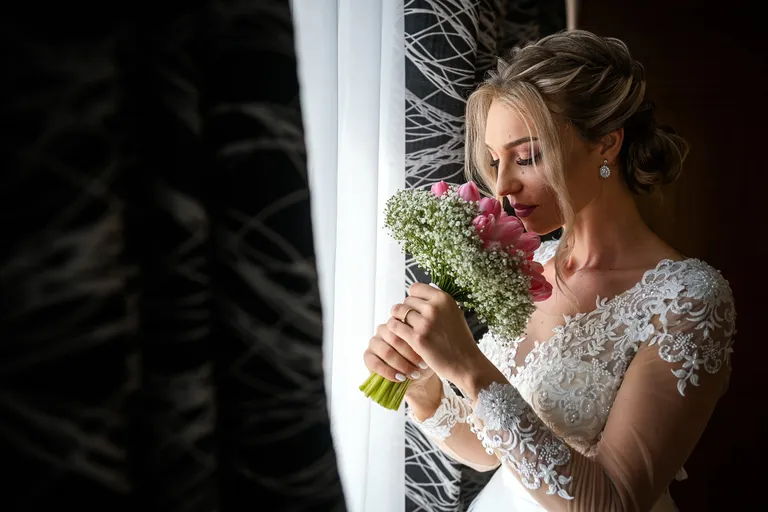 Mireasă cu buchet de flori lângă fereastră